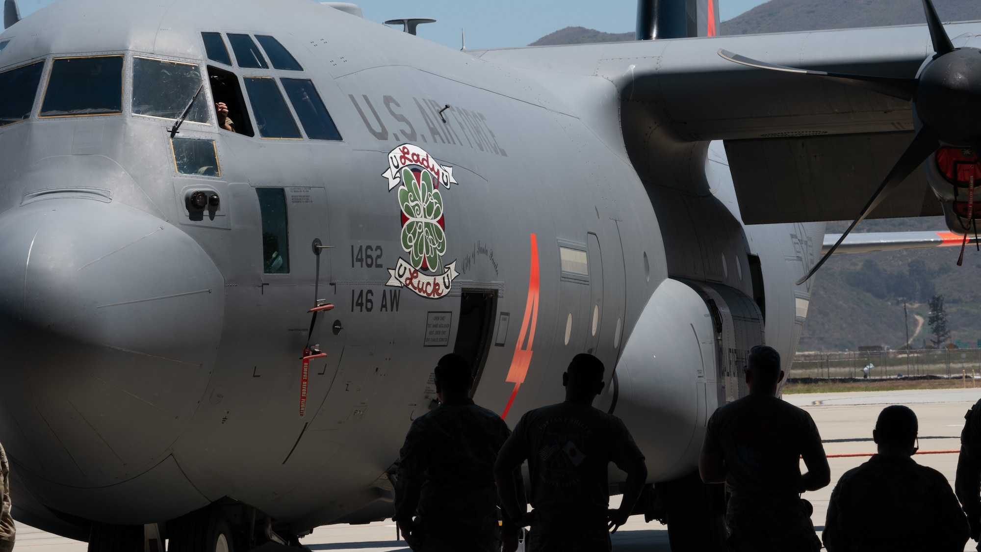 Silhouetted Air National Guard Airmen look at a large C-130J aircraft in the foreground of the photo from inside the hangar