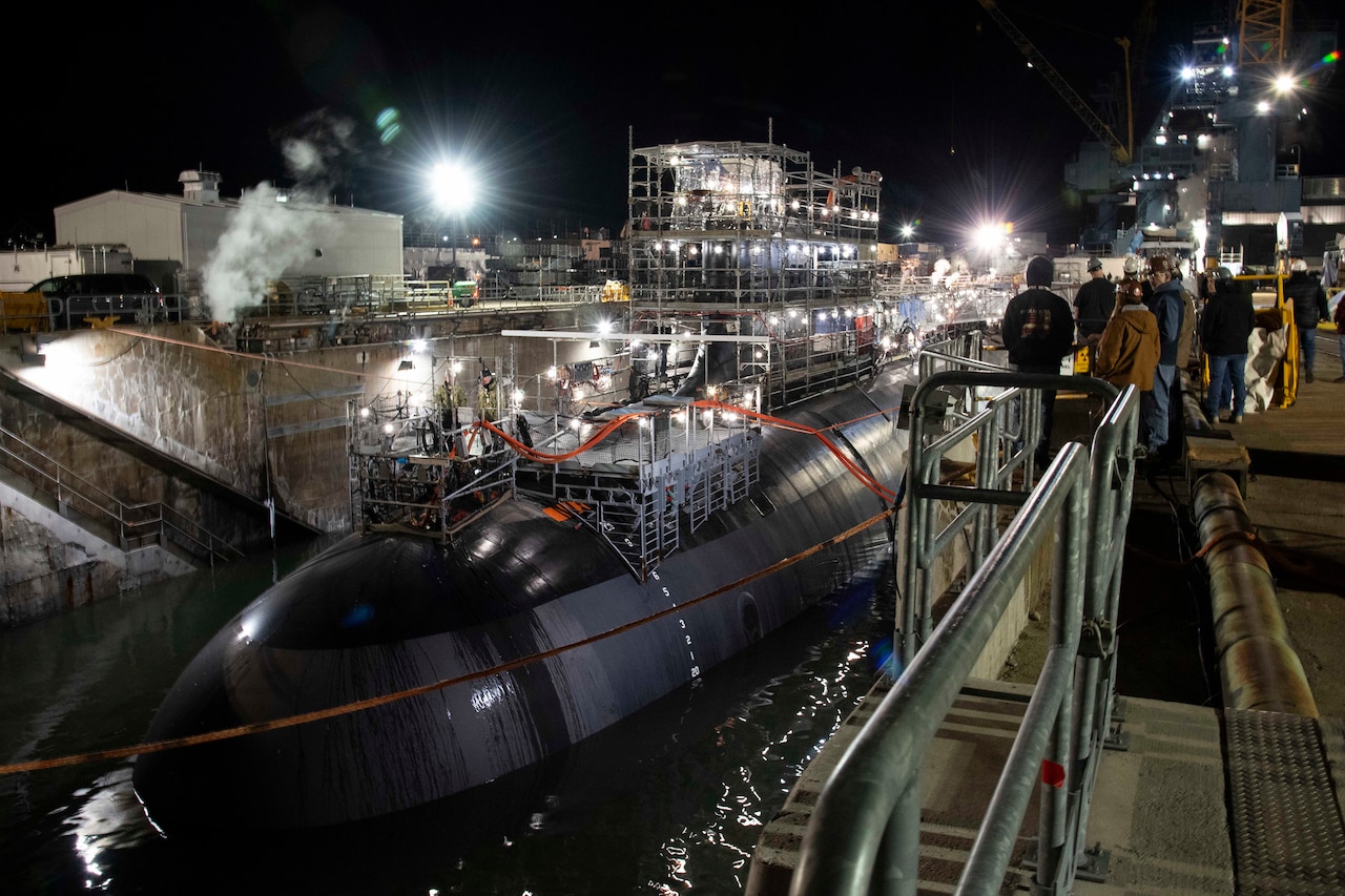 A submarine is in drydock and surrounded by scaffolding and other equipment.