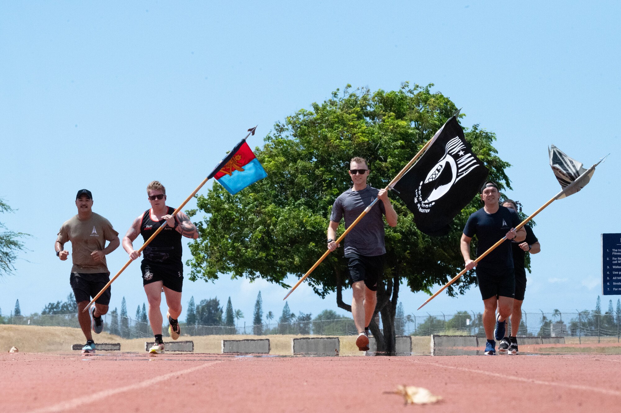 Airmen run with three flags on a track.
