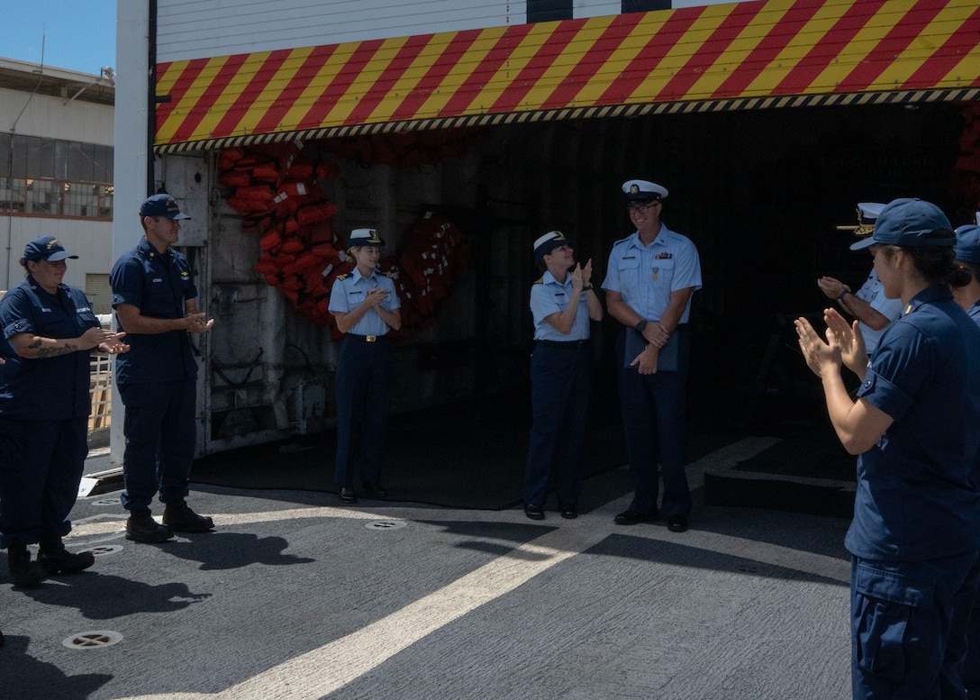 Coast Guard members stand and applaud a fellow member along the fantail of a boat.