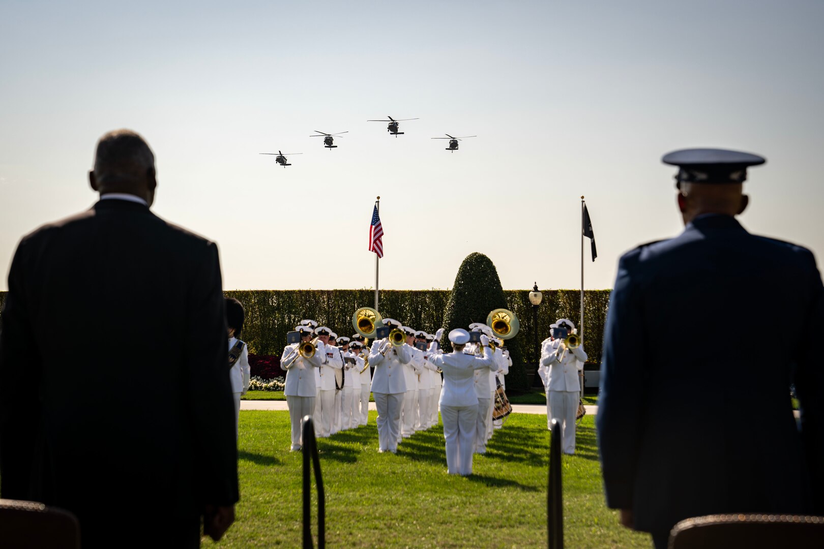 Two men face a band performing near two flags as four helicopter fly above.