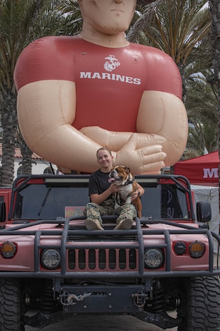 U.S. Marines Corps Cpl. Sarah Grawcock, the mascot handler and photo chief for Marine Corps Recruit Depot San Diego, and Lance Cpl. Bruno, the mascot for MCRD San Diego and the Western Recruiting Region, pose for a photo during the Super Girl Surf Pro competition at Oceanside Pier, Oceanside, California, Sept. 21, 2024. The Super Girl Surf Pro event is the only large-scale, all-women’s action sports, esports and lifestyle series in the world. The Marines participated in the event to support community relations and recruiting efforts. (U.S. Marine Corps photo by Cpl. Alexandra M. Earl)