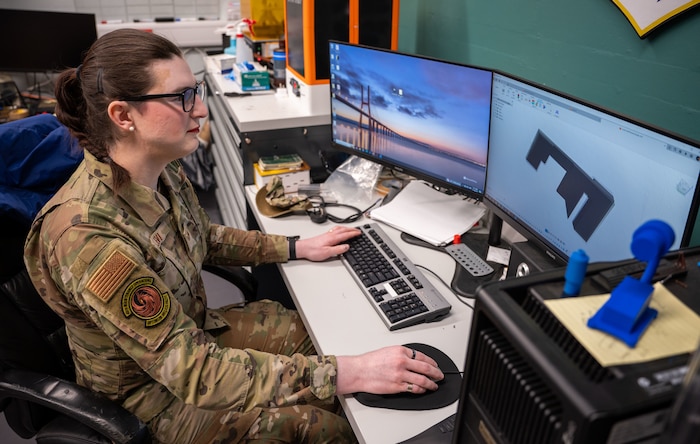 An Airman works at a computer station, uses a mouse and keyboard, and focuses on the 3D design modeling software for a project.