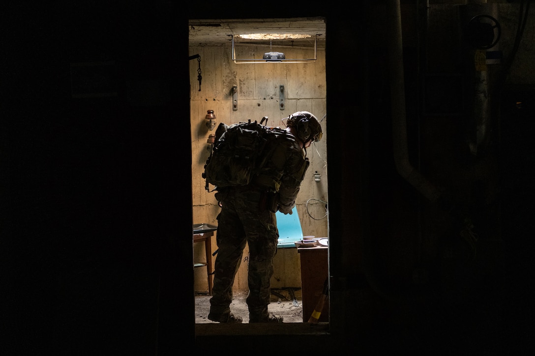 A uniformed airman wearing a helmet stands in a doorway to search for possible ordnance during a competition event.