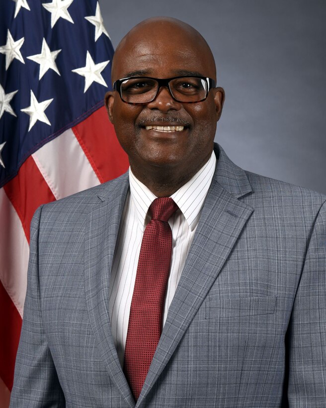 Headshot - man in gray suit and maroon tie wearing black framed glasses