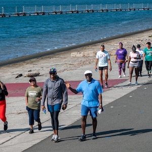 People walking alongside water to the left. Man in blue waving.