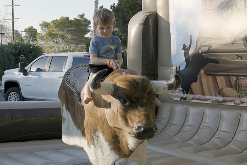 A child rides a mechanical bull outdoors.