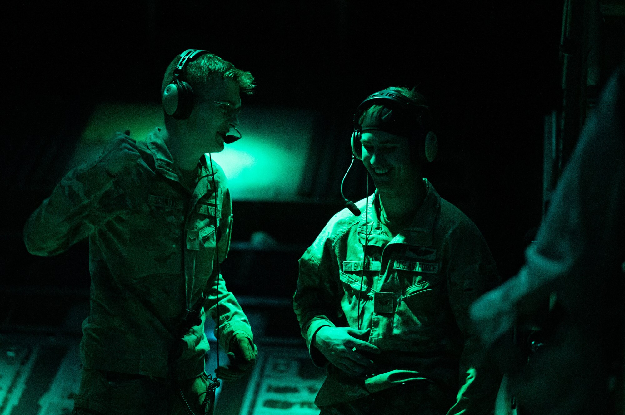 Two men in military uniform talk in a dimly lit military aircraft cabin.