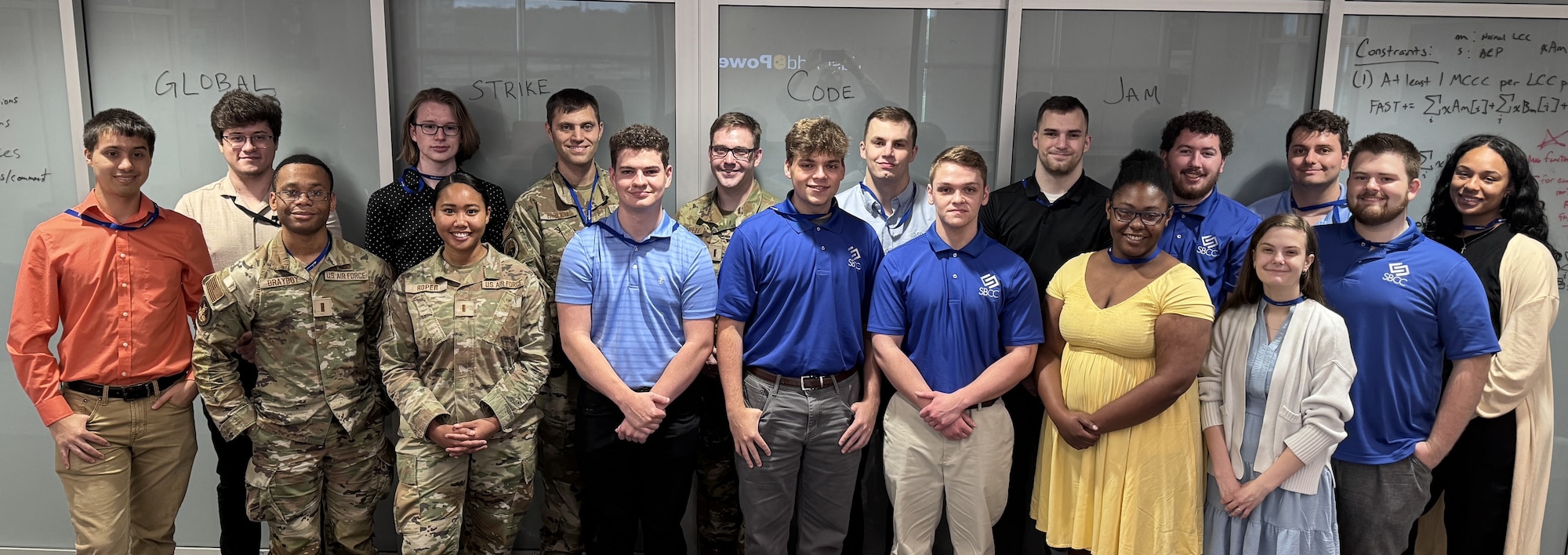People stand together and face the camera to smile for a group photo located inside an office environment.