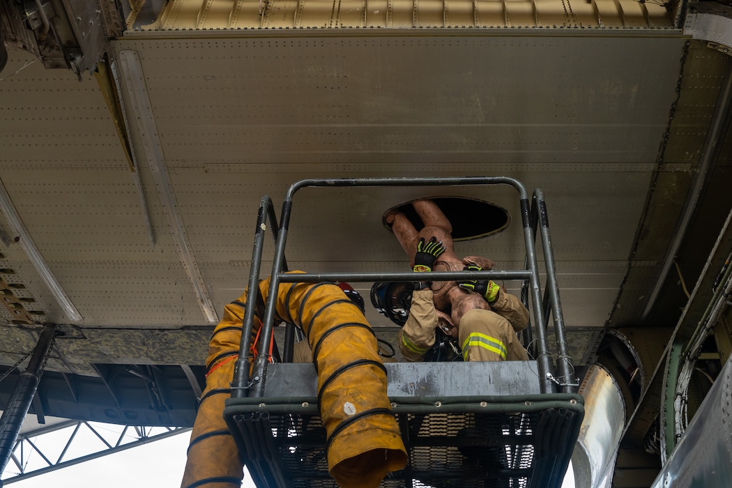 Firefighters retrieve a mannequin from a confined space in a C-130 wing cavity