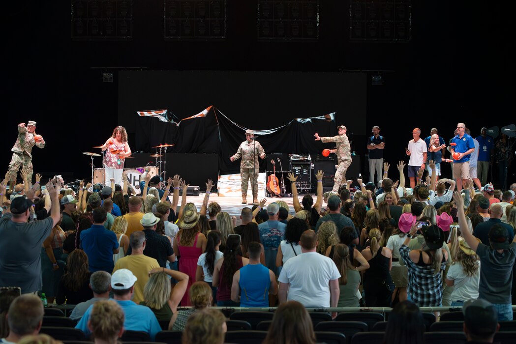 Several individuals on stage at a concert delivering opening remarks and giving away free merchandise to the crowd.