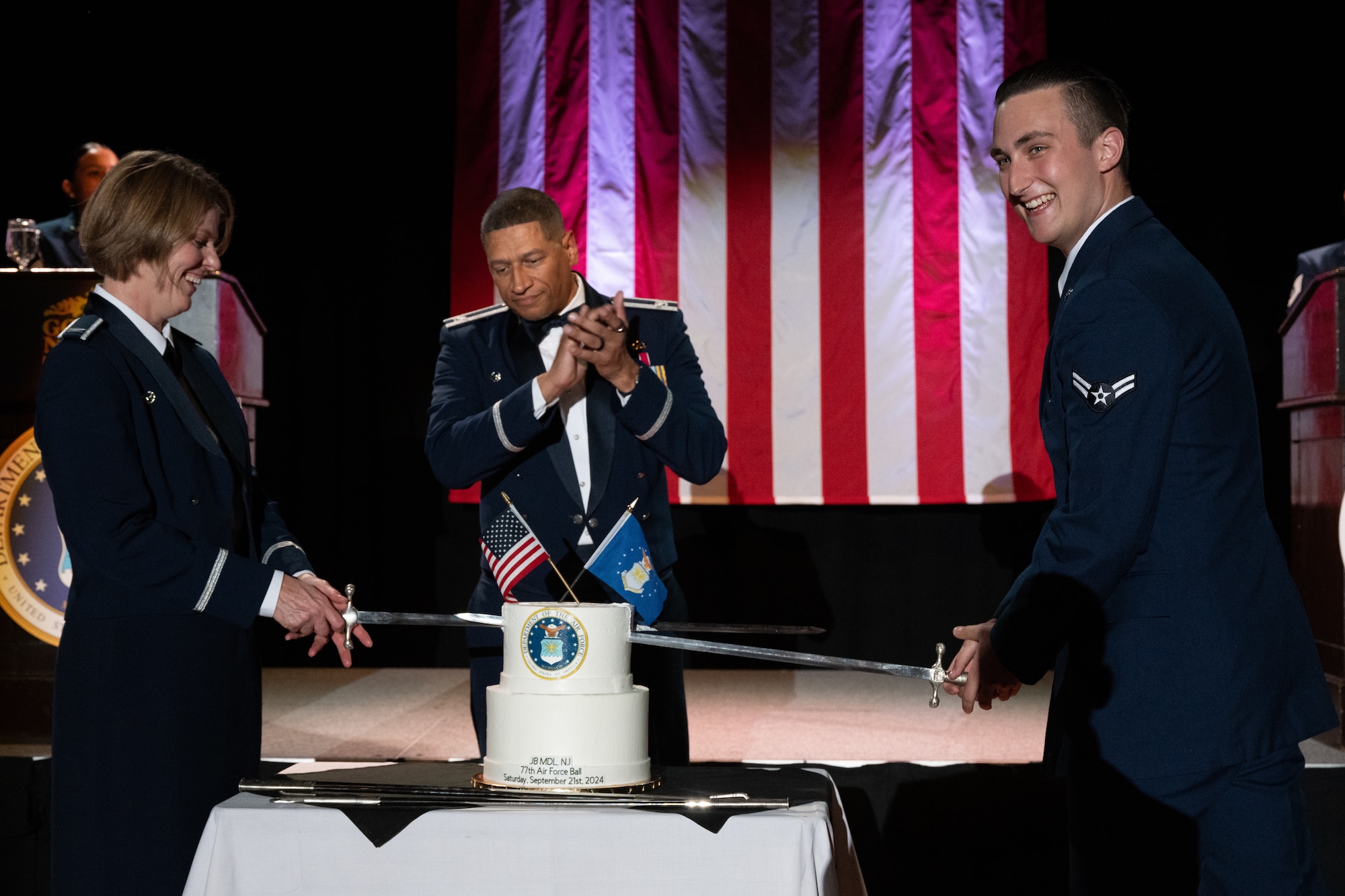 U.S. Air Force Col. Anthony Smith, Joint Base McGuire-Dix-Lakehurst commander and 87th Air Base Wing commander watches as Col. Ann D. McManis, 87th Medical Group commander, and Airman 1st Class Jason Mickelson, 87th Logistics Readiness Squadron fuels distribution operator service center controller, cut a cake during the U.S. Air Force Ball in Atlantic City, N.J., Sept. 21, 2024. The annual event honors the U.S. Air Force’s heritage of air and space dominance. (U.S. Air Force photo by Senior Airman Aidan Thompson)