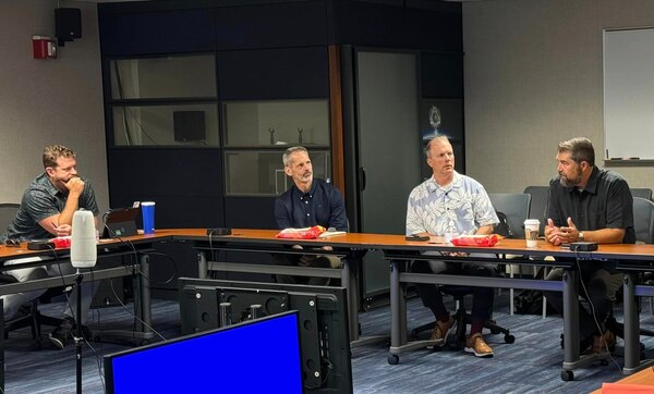 Director Lopez sits at conference room table, speaking to other leaders who are also seated at conference room tables.