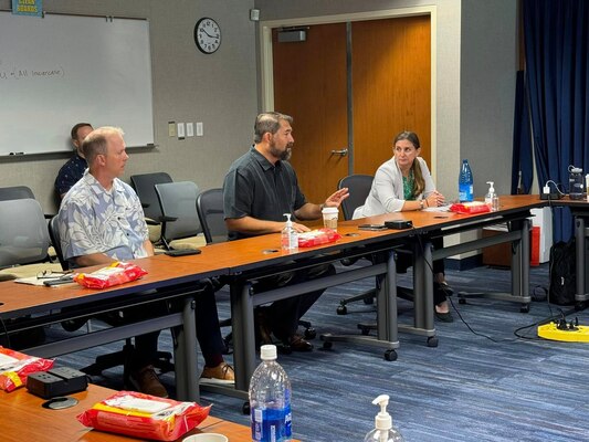 Director Lopez sits at conference room table with others looking on while discussing NCIS mission.