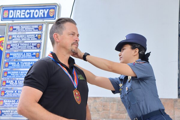 NCIS Special Agent receives medal around his neck by female Manila Police member.