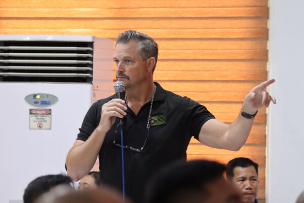 NCIS Special Agent holds microphone while speaking to Manila police members.