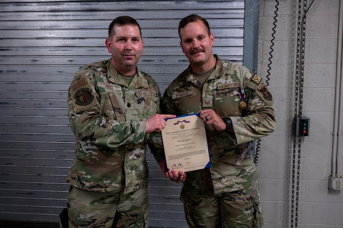 Tech. Sgt. Seth Phares stands on the right side of the photo holding his certificate of award for the Air Medal posing for the camera