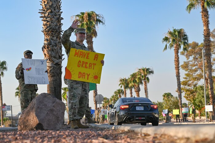 Airmen wave to drivers while holding encouraging signs during a Suicide Prevention Awareness Month base wave-in