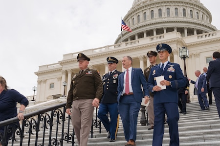 Five men are walking down the steps outside the U.S. Capitol. Four are in military uniforms and one is in a business suit.