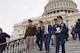 Five men are walking down the steps outside the U.S. Capitol. Four are in military uniforms and one is in a business suit.