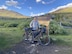 A man stands with his bicycle in front of a large yellow and brown sign that reads "Boreas Pass."  behind him are rolling hills.