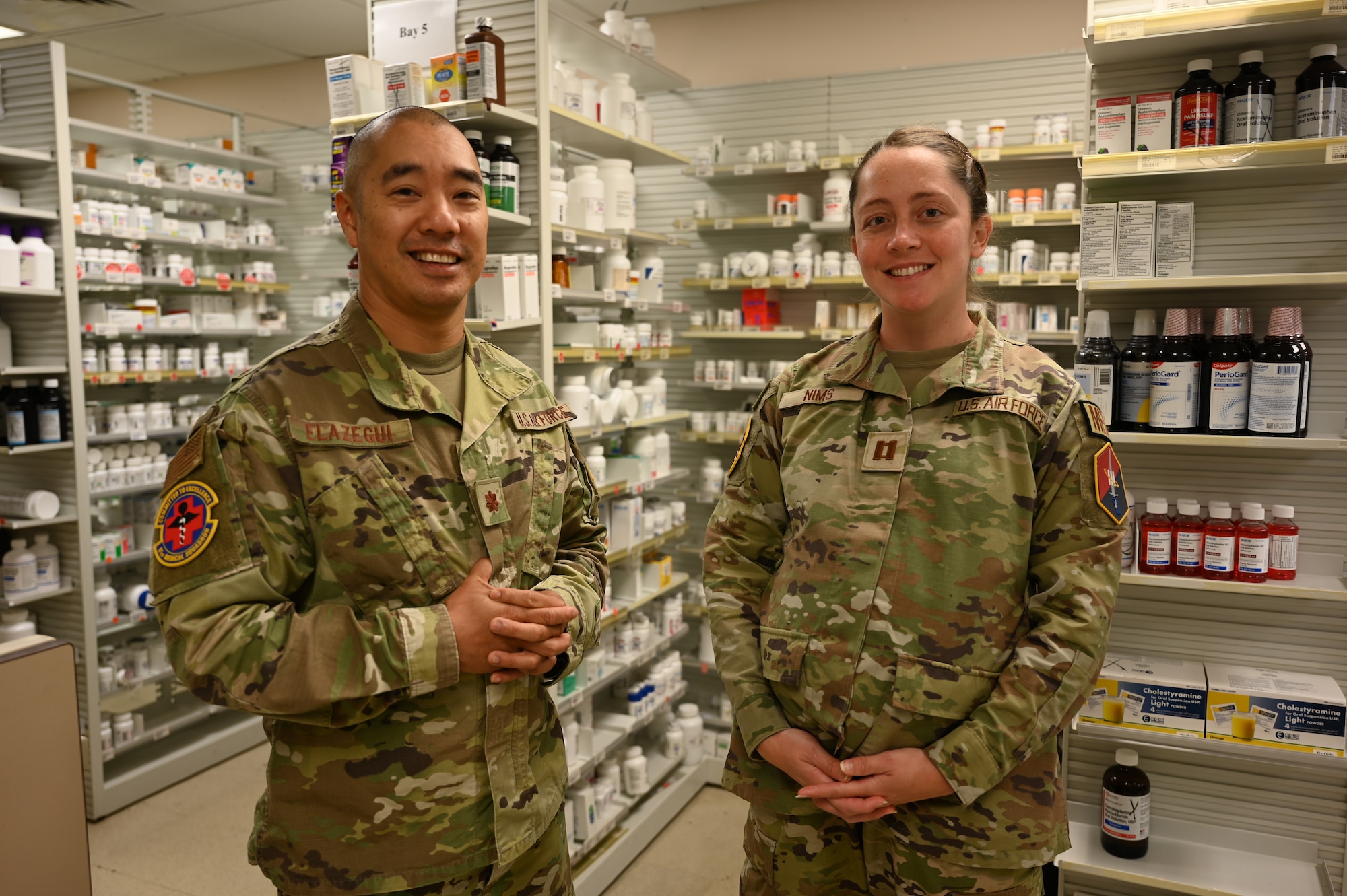 Flight Commander Maj. Ronald Elazegui and Pharmacy Element Chief Capt. Xrystina Nims of the 61st Medical Squadron (MDS), Space Base Delta 3 at Los Angeles Air Force Base (LA AFB) stand in the pharmacy, surrounded by shelves of medications. (U.S. Space Force photo by Amy Urbina).