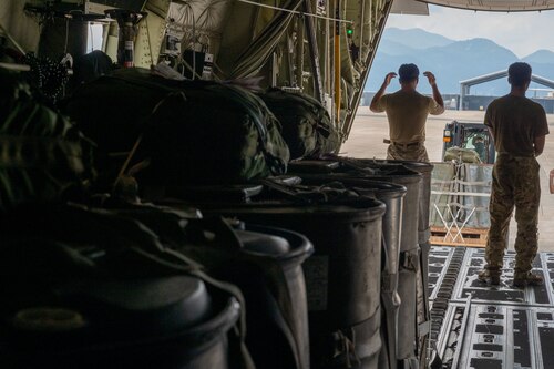 Cargo in the foreground and military members marshalling a forklift.