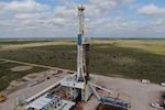 Photo of a test well on a dirt foundation, in the middle of a grassy field