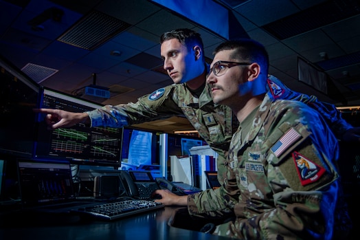  Two U.S. Space Force Guardians check a computer monitor in a dark room.