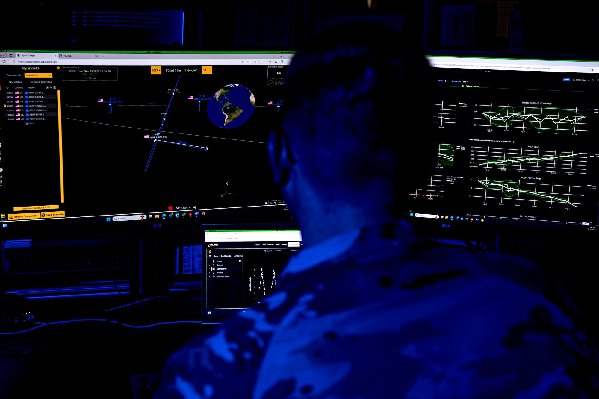 A man in uniform looks at computer displays of data in a dark room.