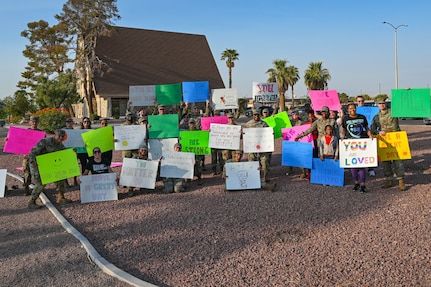 Service members in uniform and people wearing civilian clothes hold signs with encouraging phrases.