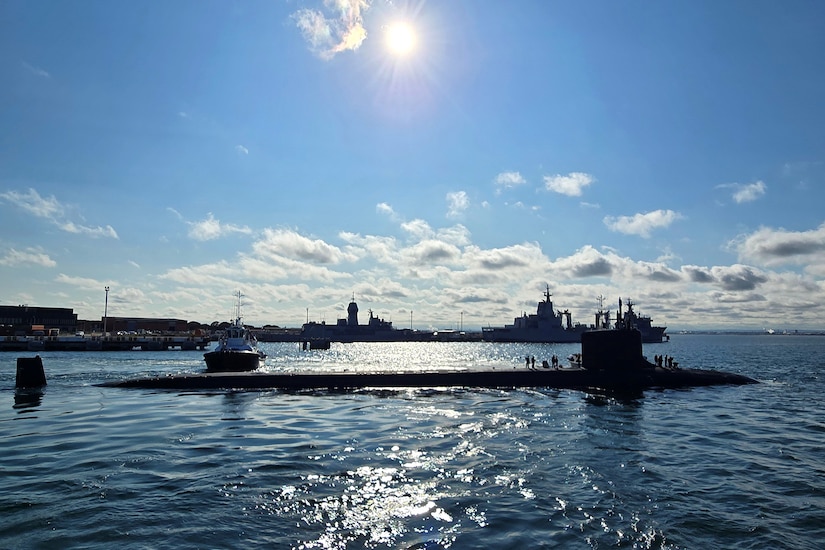 A submarine is part of the way above water during a sunny day by a dock.