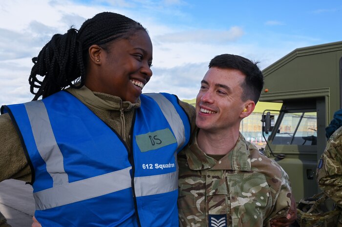 Senior Airman Faramade Adeyemi, left of frame, laughs with Sgt. John Hogan, right of frame, in solidarity as they embrace shoulder to shoulder