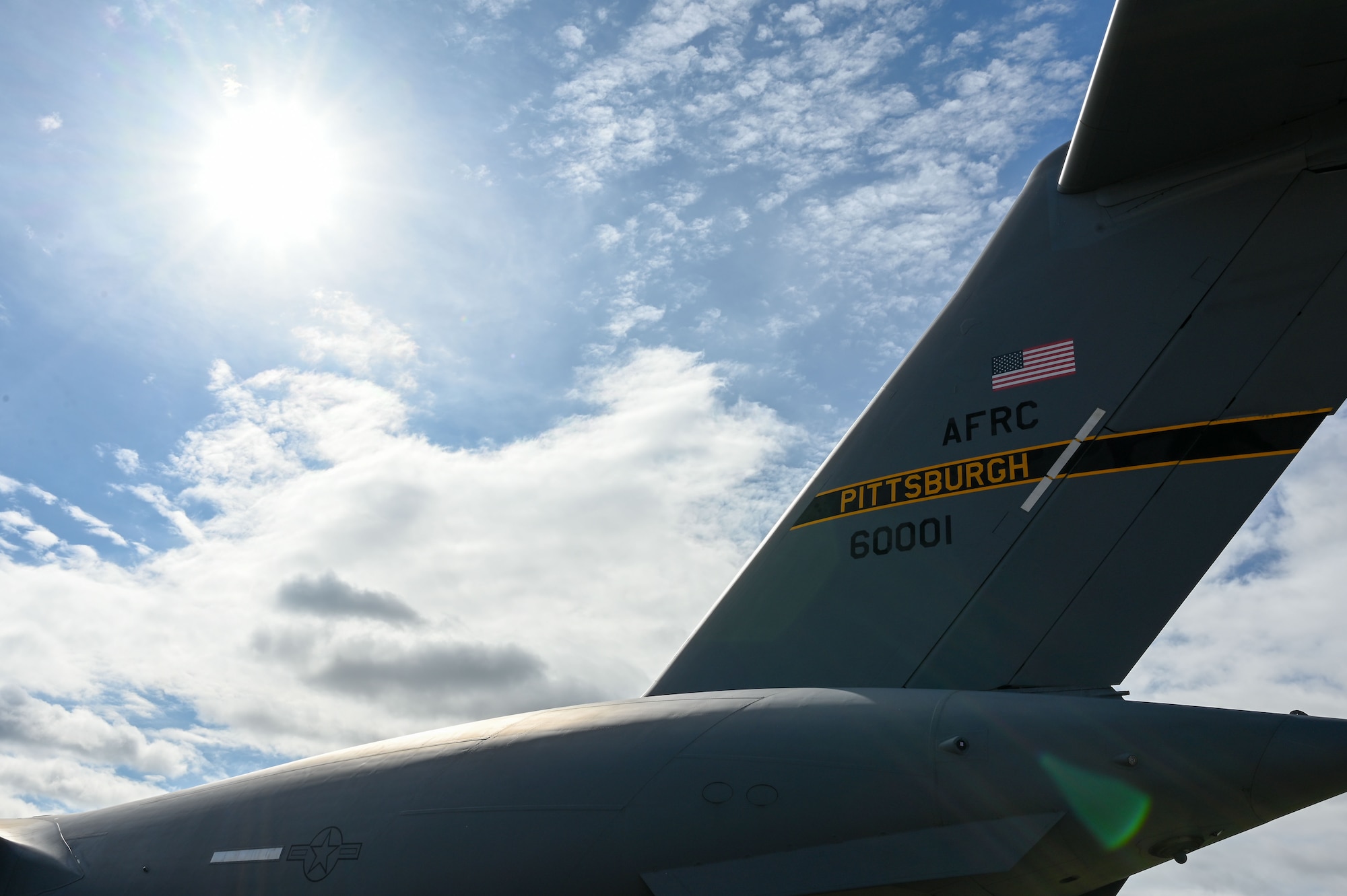 The tail of one of 911th Airlift Wing's C-17 Globemaster III fills the right side of the frame with a cloudy sky and sunlight filling the left frame