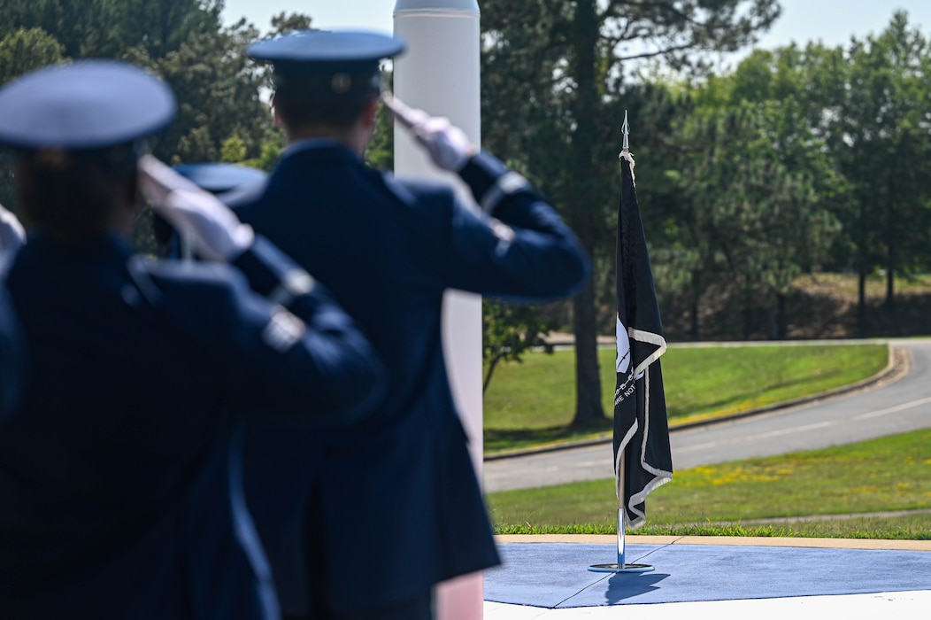 Personnel in uniform salute a POW/MIA flag during a ceremony.