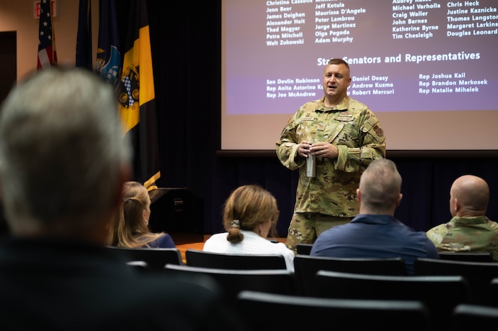 Col. Stouffer stands at the front of a briefing room providing a presentation to an audience in the foreground