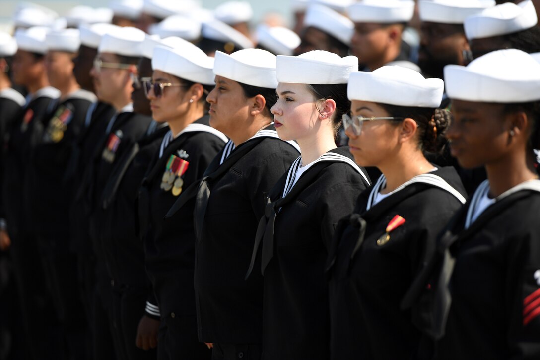 Sailors stand side-by side in multiple rows during daylight.