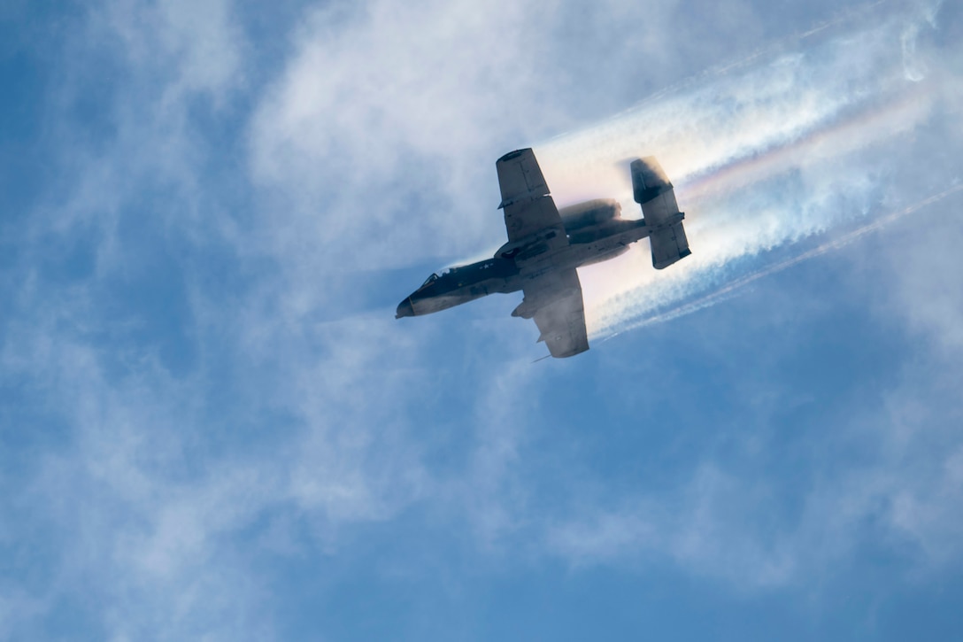 An aircraft leaves streaks in the sky as it moves across a cloudy, blue sky.