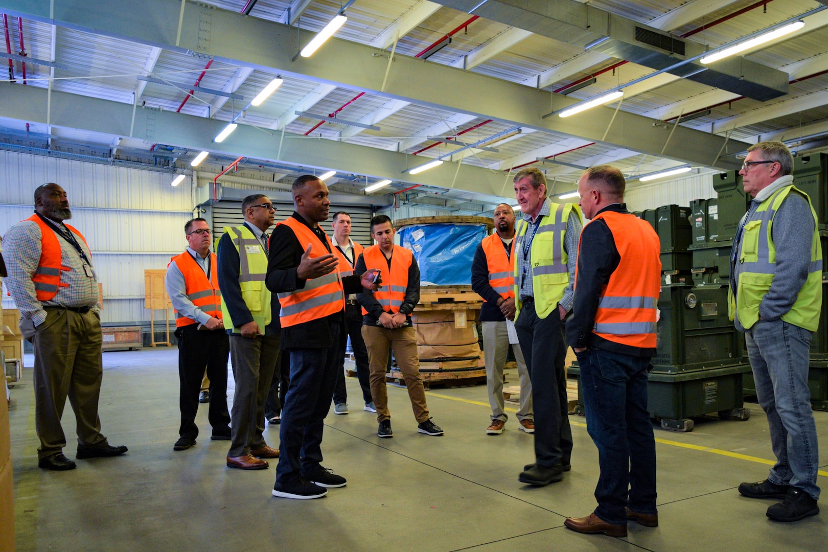 A group of people in reflective vests stand talking in a warehouse.