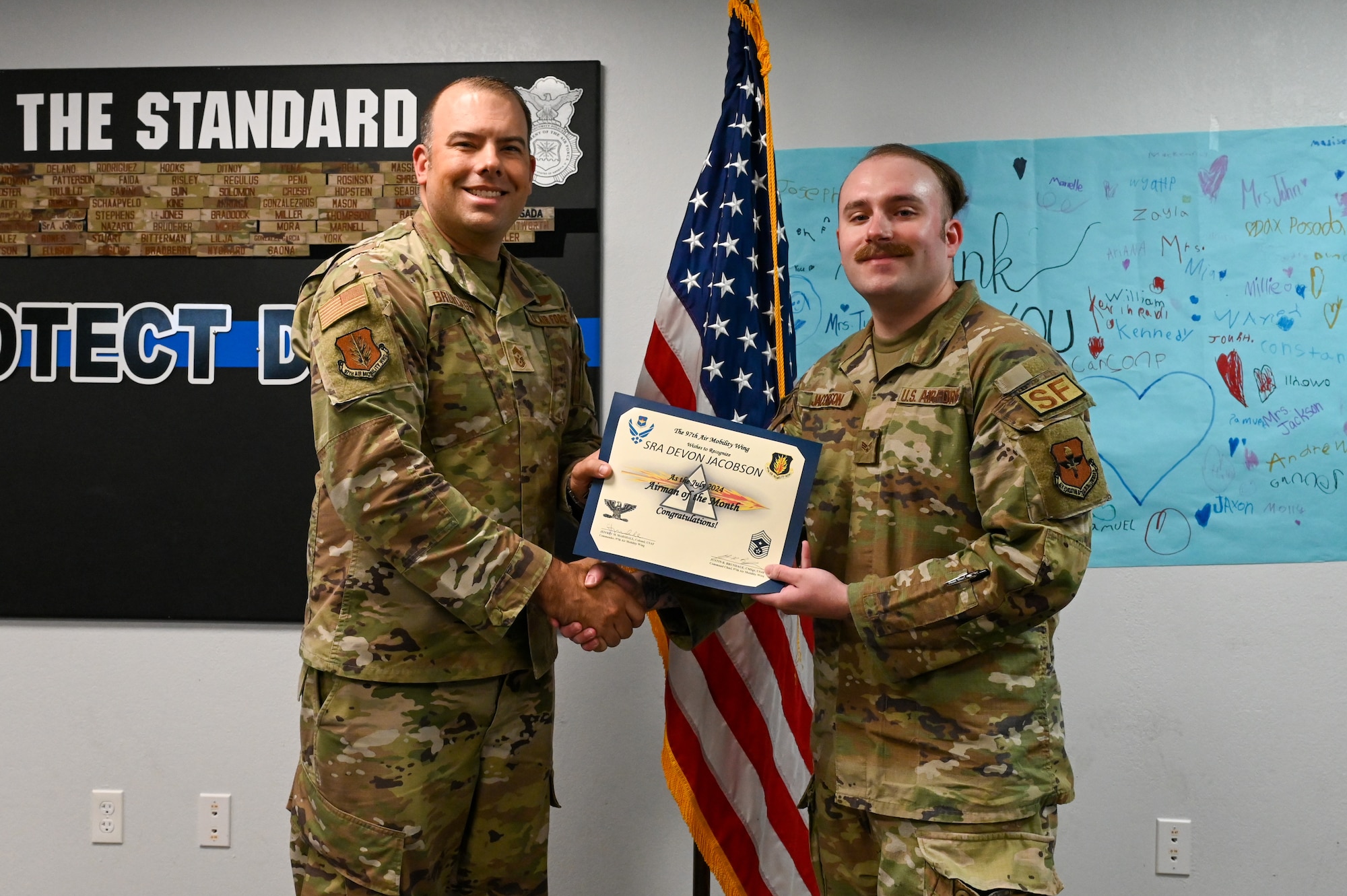 U.S. Air Force Chief Master Sgt. Justin Brundage, 97th Air Mobility Wing command chief, awards the July Airman of the Month certificate to Senior Airman Devon Jacobson, 97th
Security Forces Squadron patrolman, at Altus Air Force Base (AFB), Oklahoma, September 16, 2024. Jacobson was chosen due to vigilance and care when helping Airmen, as well as his efforts to ensure the safety of Altus AFB residents. (U.S. Air Force photo by Senior Airman Kari Degraffenreed)