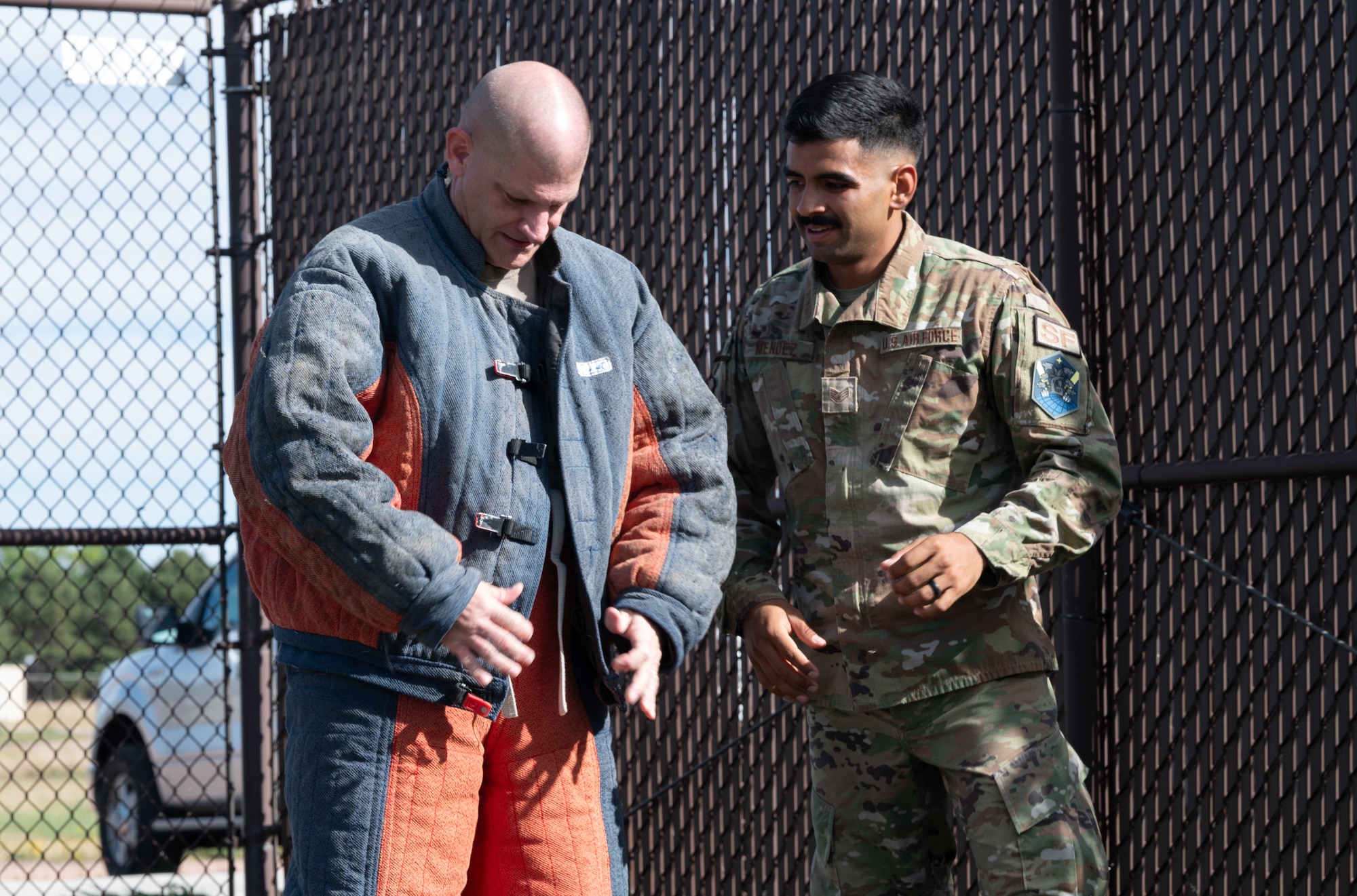 U.S. Air Force Staff Sgt. Ivan Mendez, 21st Security Forces Squadron military working dog trainer, helps U.S. Space Force Col. Kenneth Klock, Space Base Delta 1 commander into a protective suit designed to train military working dogs.