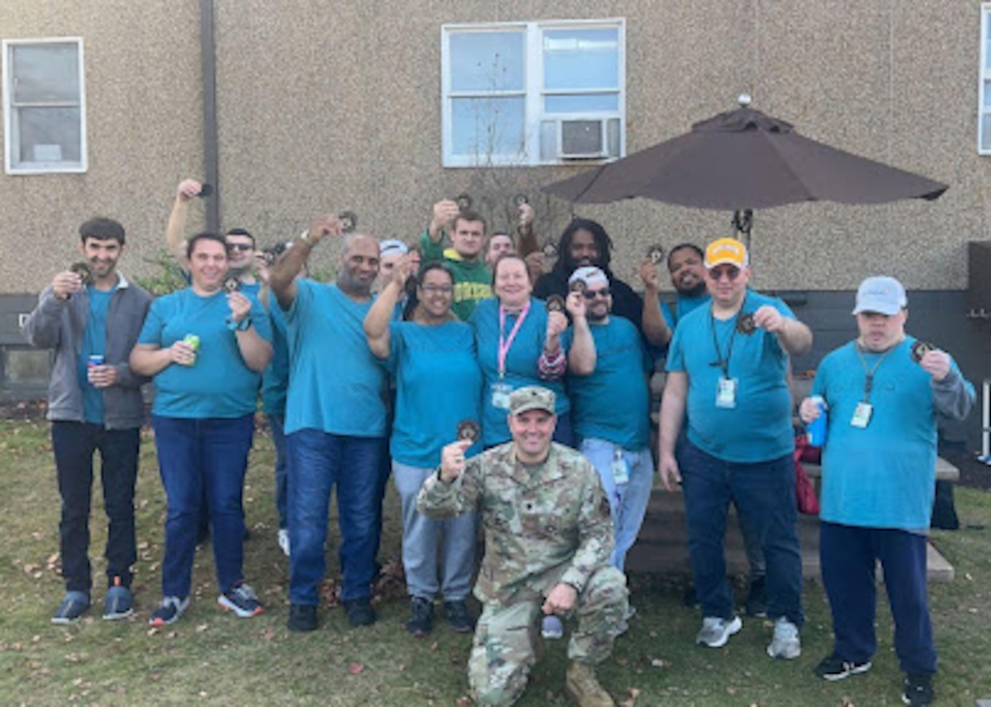 Members of the Achieva custodial staff pose for a photo holding coins behind Lt. Col. Reid who is kneeling in the foreground