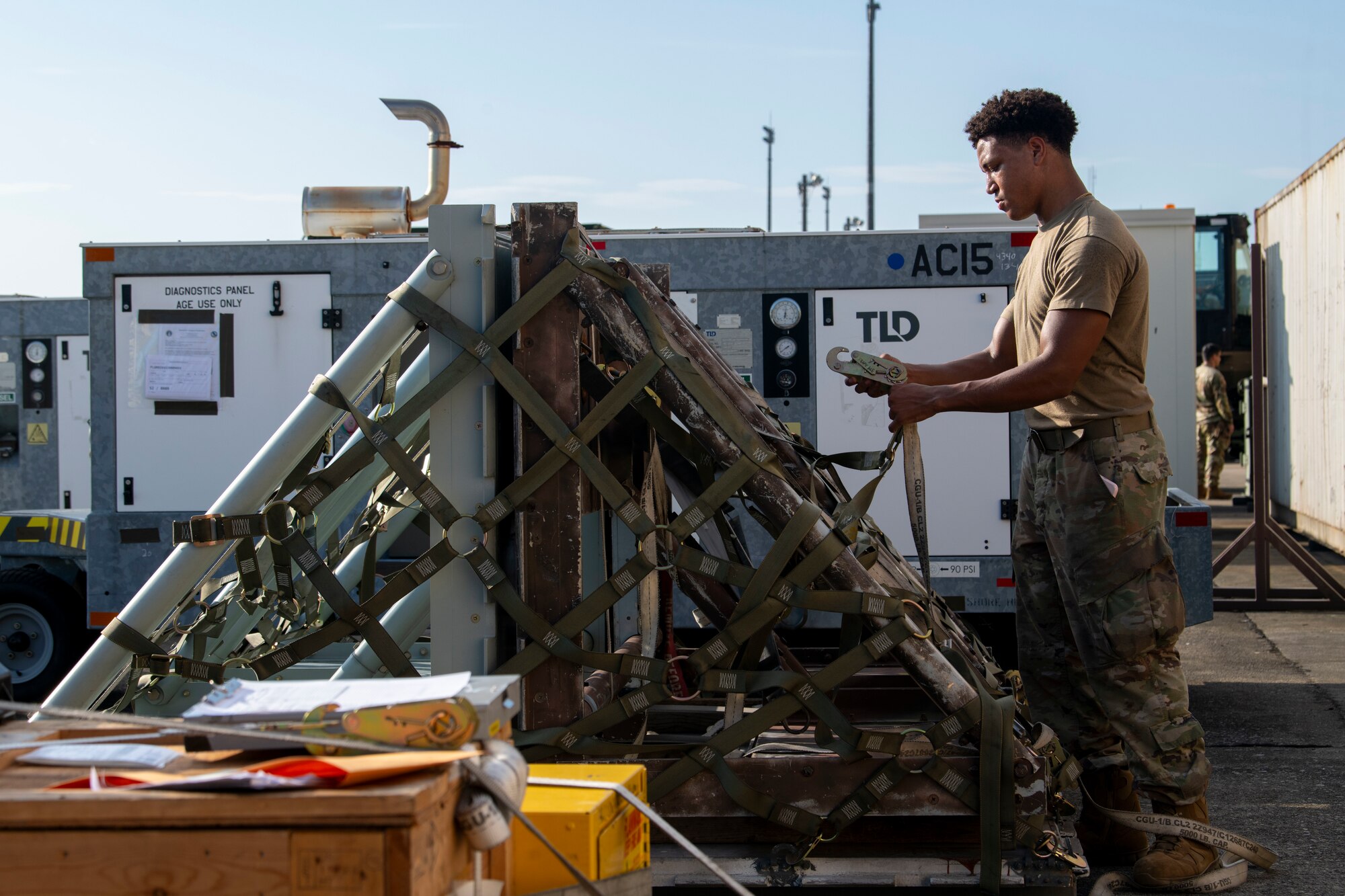 A military member prepares to attach a hooked harness to a piece of equipment.