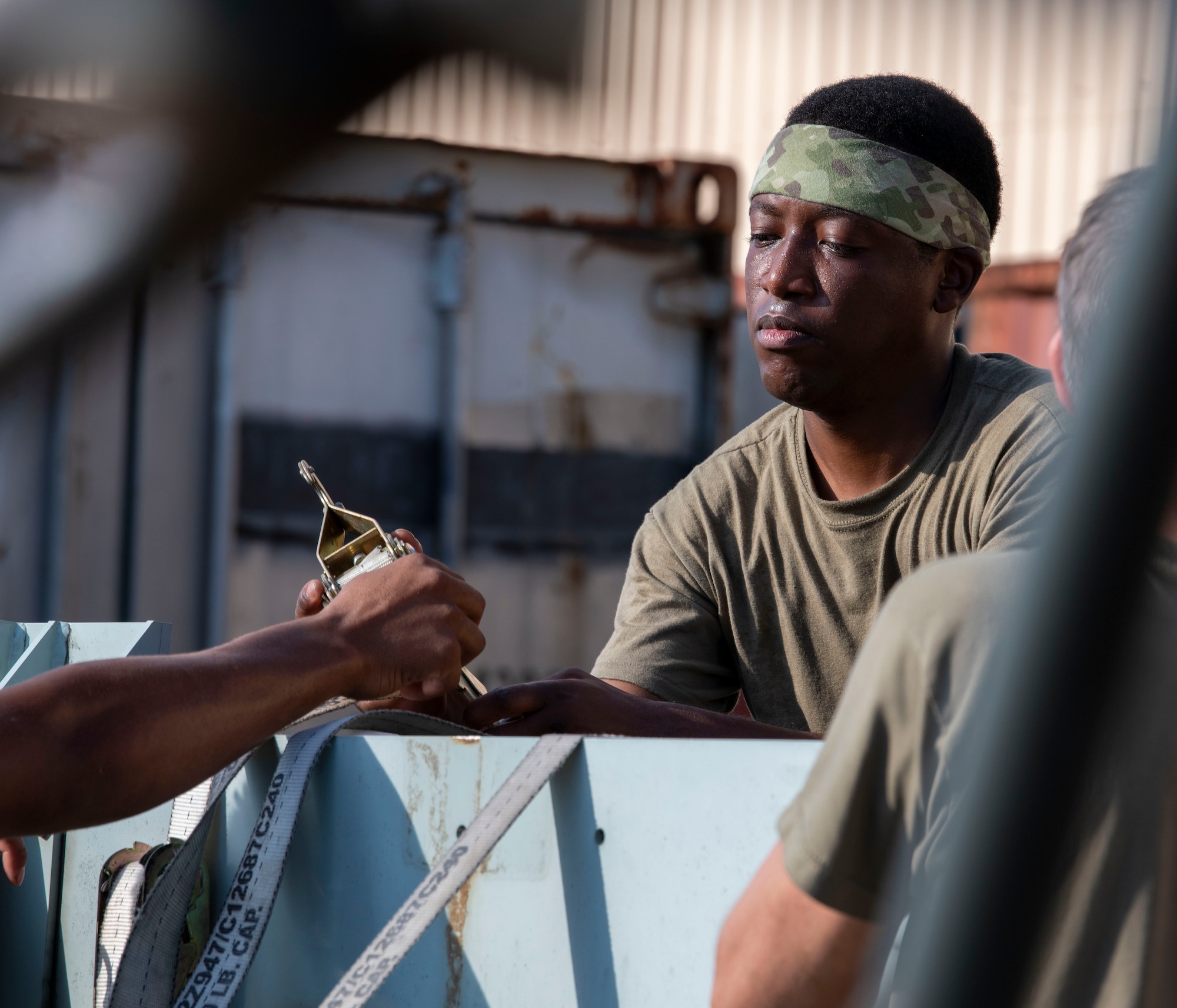 A military member attaches a harness strap to a piece of equipment.