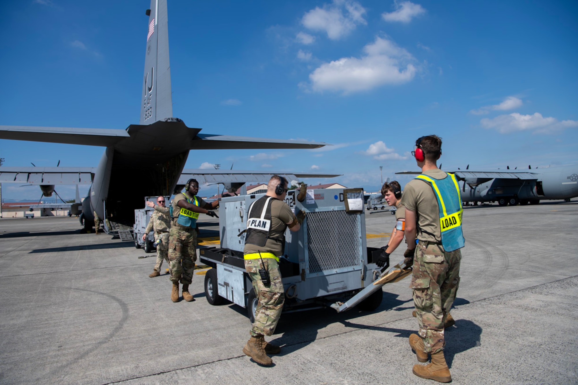 A group of Airmen push a generator towards the back of an aircraft.