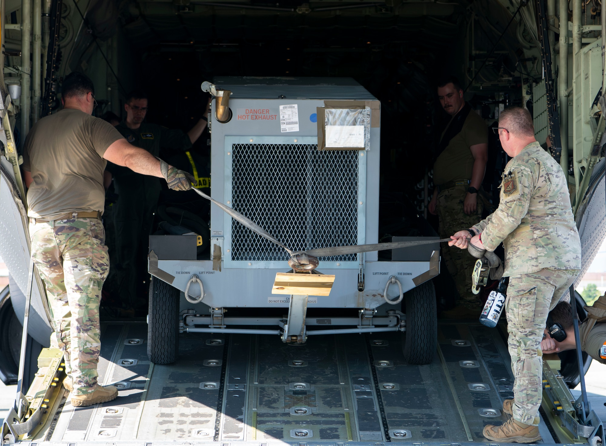 Two military members pull a generator on to the back of an aircraft.