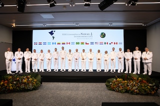 A group of naval personnel in white uniforms posing in a line for a photo.