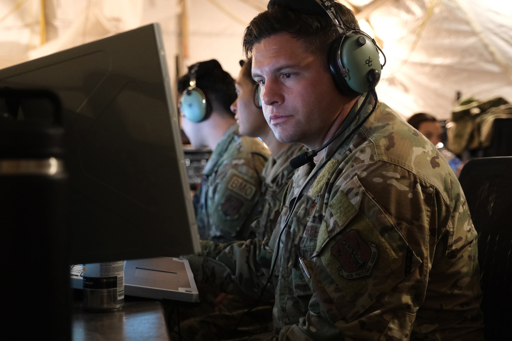US Air Force Airmen wearing headphones work on computers