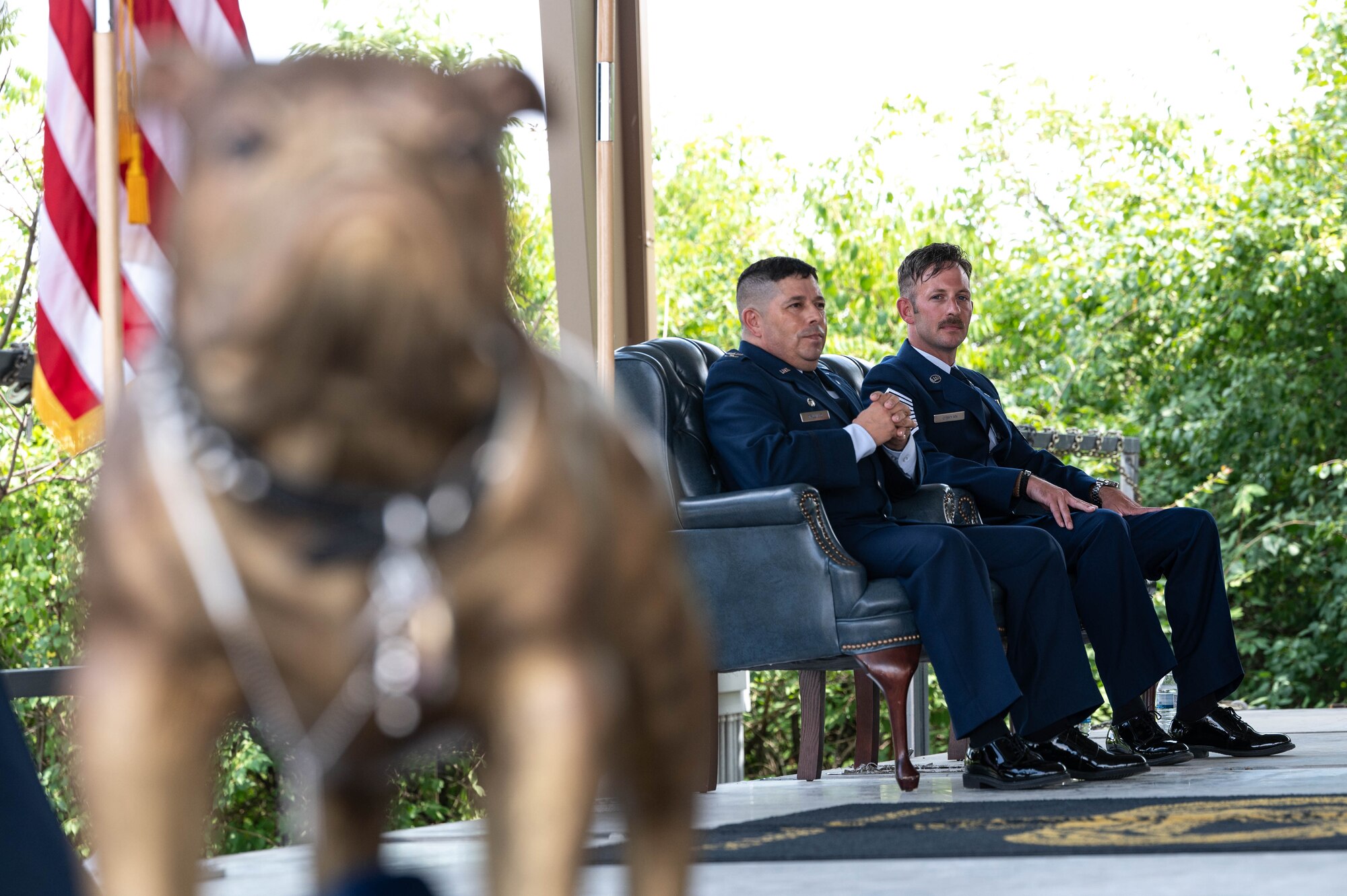 Col. Reginald Trujillo and Chief Master Sgt. Patrick O'Bryan sit in the background right of frame with the blurry Sheppard's Trophy in the foreground left of frame