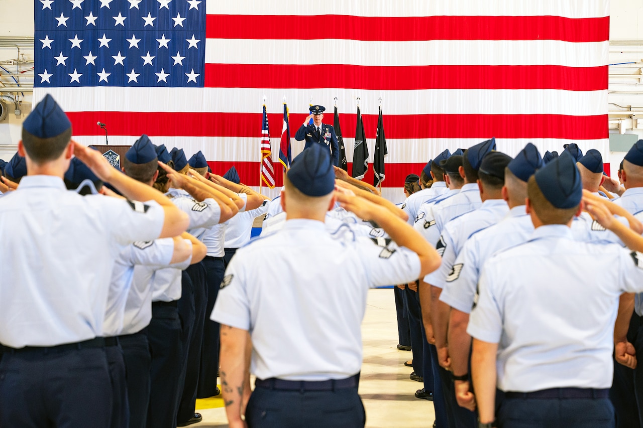 A squadron of guardians salute the American flag and a commanding officer on a platform who salutes back at the guardians.